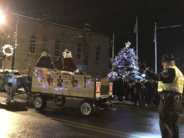 Horse-drawn wagon decorated with lights at a nighttime Christmas event.