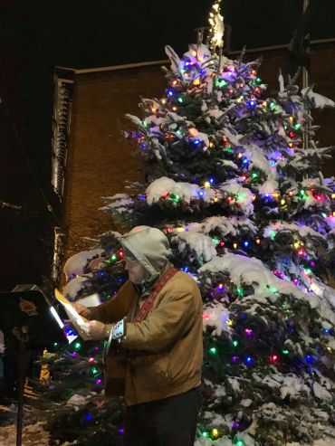 Man playing guitar by a snow-covered, decorated Christmas tree at night.