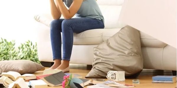 A woman sitting on a couch holding her head in distress.