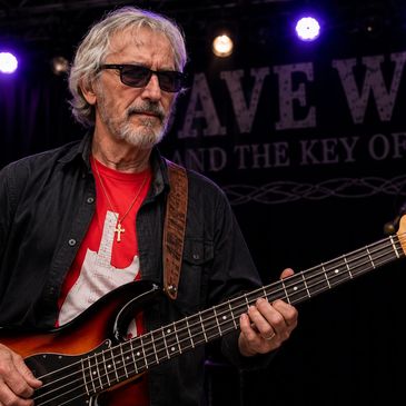 Older man playing bass guitar on stage.