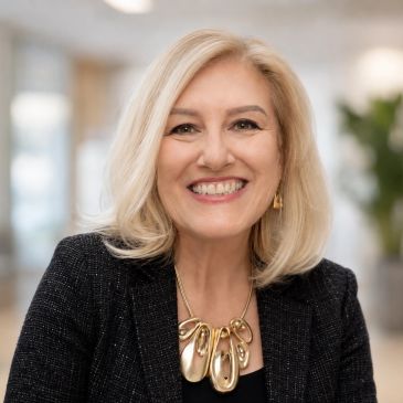 Smiling woman with blonde hair and gold necklace.