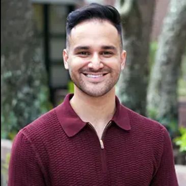 Smiling man in a maroon sweater outdoors.