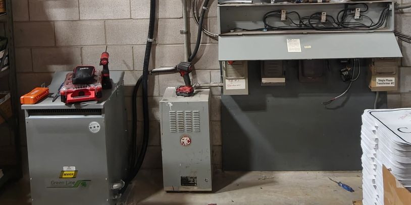 Industrial workspace with electrical panels and tools on the floor and surfaces.