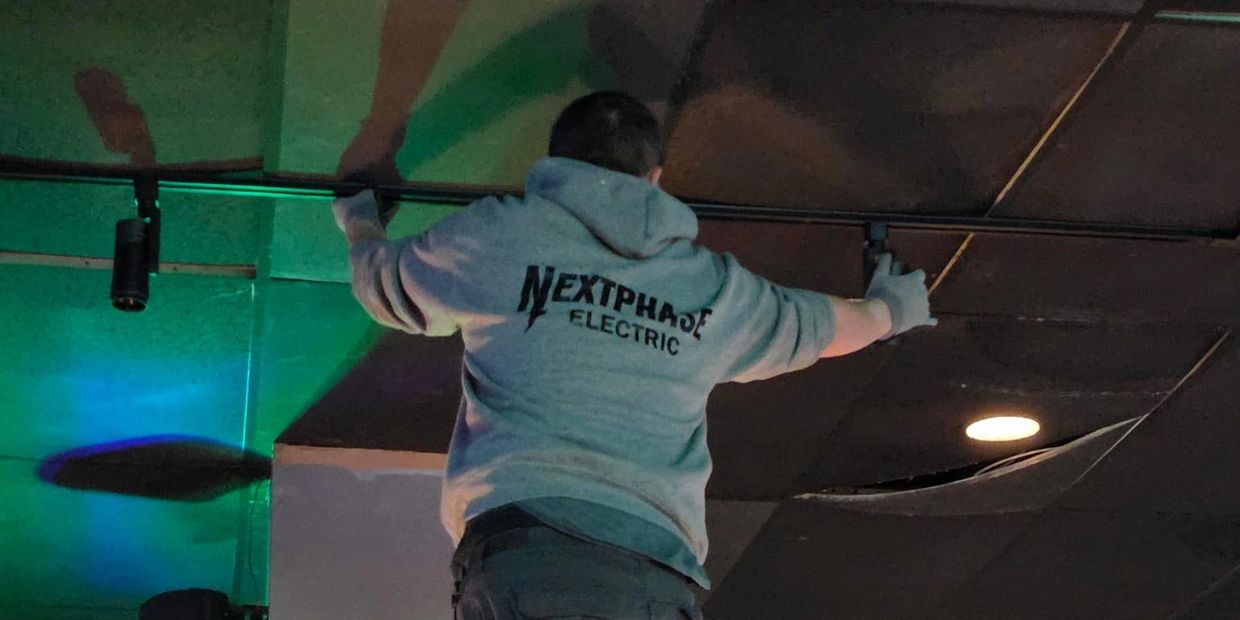 electrician services Markham. Electrician on ladder fixing ceiling lights in a dimly lit room.