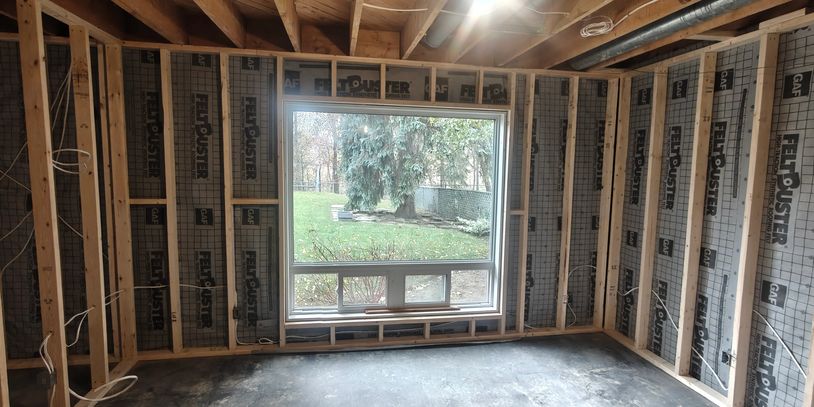 Room under construction with exposed framing and a large window looking outside.