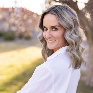 Woman smiling outdoors with wavy hair and white shirt.