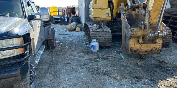 Excavator and pickup truck on a dirt lot at a worksite.