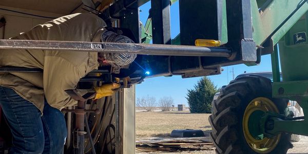 Person welding a tractor part with protective gear.