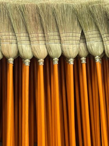 A row of neatly arranged traditional brooms with orange handles.