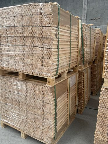 Stacks of wooden dowels neatly packed on pallets in a warehouse.