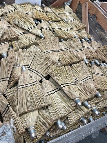 A pile of traditional hand brooms made of natural straw.
