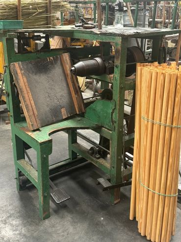 A green industrial machine with wooden sticks bundled beside it.