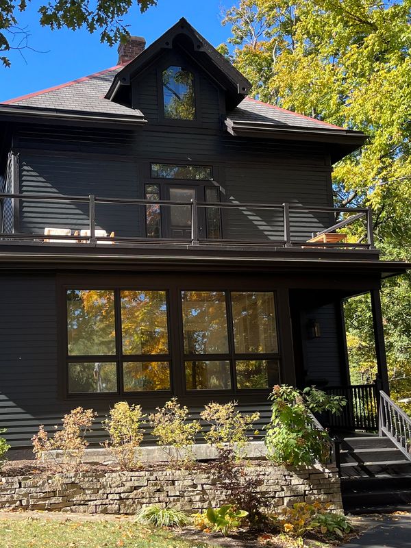Black house with a balcony surrounded by trees.