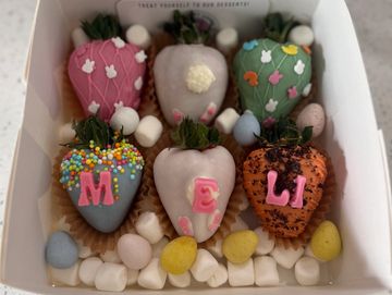 Colorful chocolate-covered strawberries spelling 'MELI' with decorative sprinkles and marshmallows.