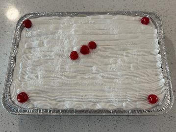 Rectangular cake with white frosting and cherries on top in an aluminum tray.