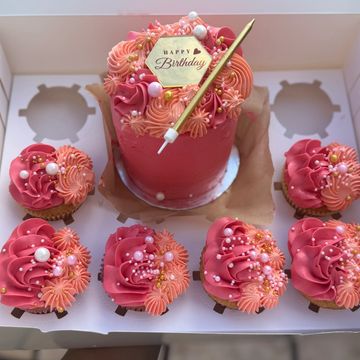 Pink birthday cake with matching cupcakes decorated with pearls and flowers.
