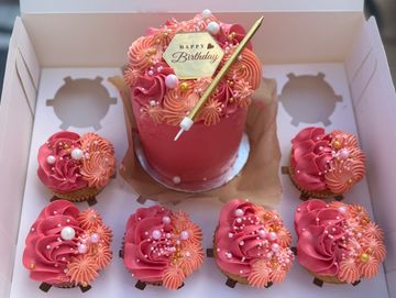 Pink birthday cake with matching cupcakes decorated with pearls and flowers.