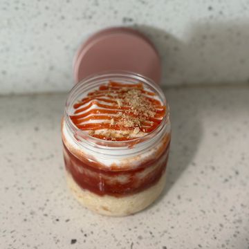 Layered dessert in a jar with cream, sauce, and crumbs.