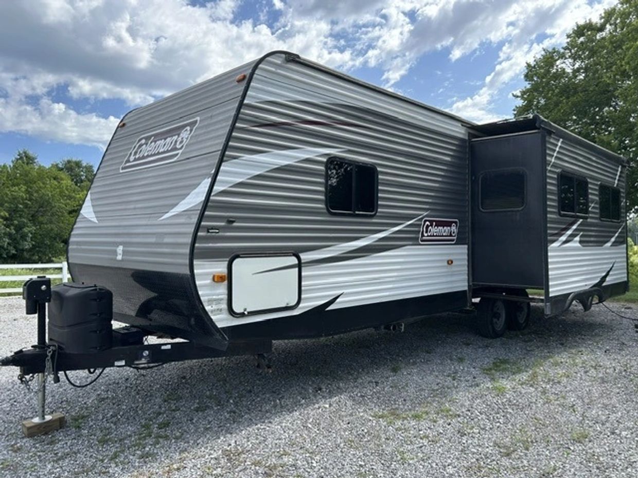 Gray Coleman travel trailer parked on gravel.