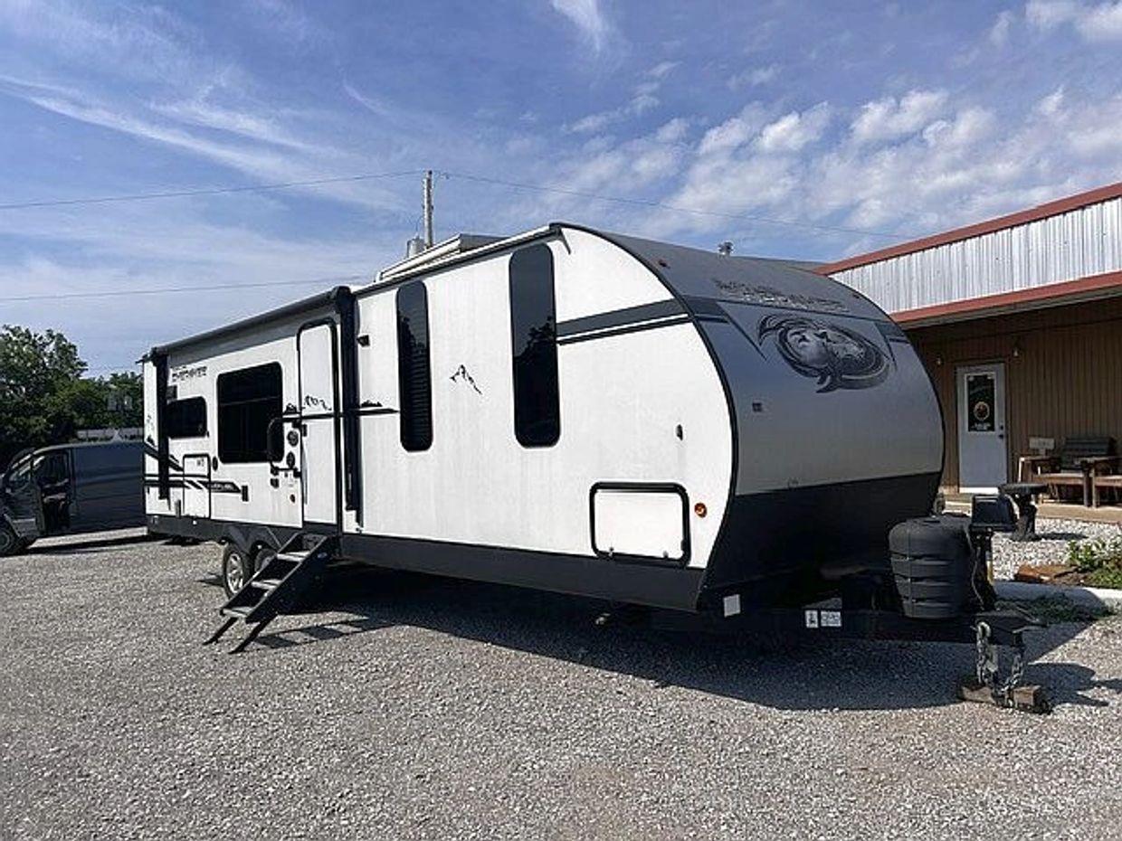 White and black travel trailer parked on gravel under a partly cloudy sky.