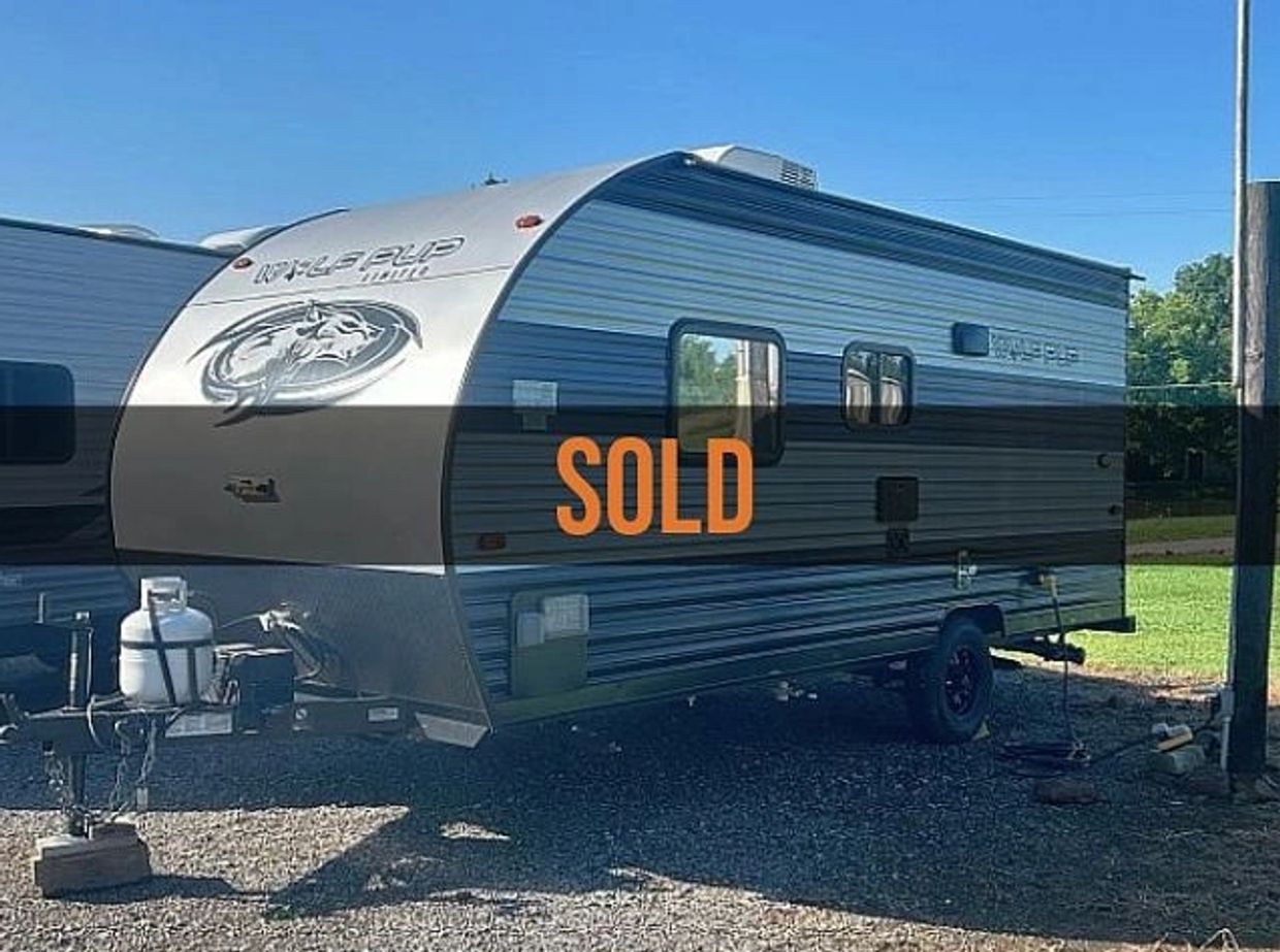 A sold Wolf Pup travel trailer parked outdoors on gravel under clear blue sky.