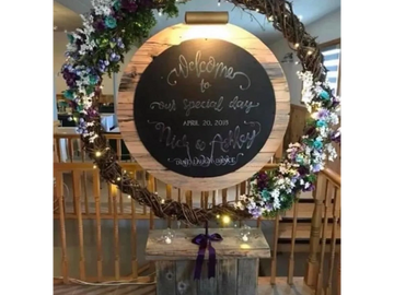 Circle chalkboard sign with grapevine that lights up and rustic wooden base displayed at a hall