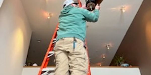 Person on a ladder fixing a ceiling fixture in a modern room.