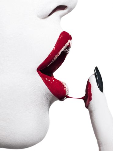 Close-up of lips with red paint and matching painted finger.