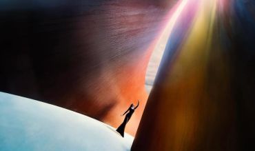 Silhouette of a person reaching up between large curved structures with sunlight.