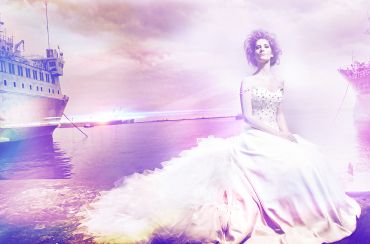 Woman in a white dress sitting by the water at sunset.
