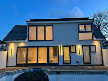 Modern white house with large windows and exterior lights at dusk.
