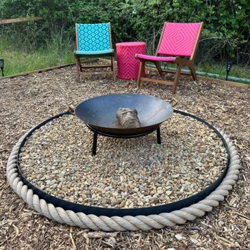 Outdoor fire pit surrounded by chairs with colorful cushions in a garden.