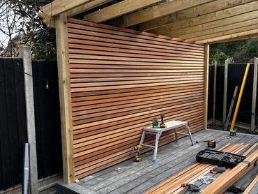 cedar slat wall has gone up, composite decking is down and pergola frame and roof is on. 