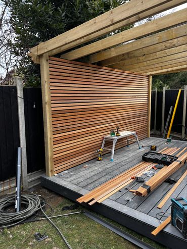 cedar slat wall has gone up, composite decking is down and pergola frame and roof is on. 