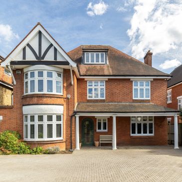 Large traditional brick house with white-framed windows and a tiled roof.