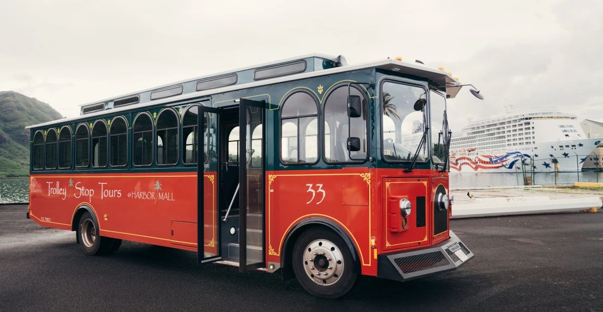 Red trolley bus for tours at a harbor with cruise ship in background.