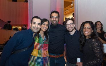 A group of five friends smiling at a social event indoors.