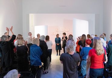 Audience applauding two women standing in a gallery or presentation space.