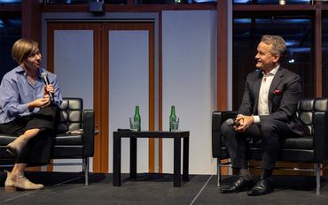 Two people sitting on stage having a discussion with microphones.