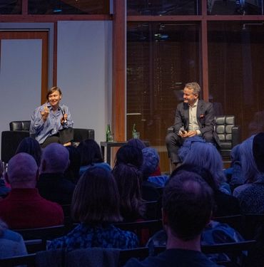Two people engaged in a discussion on stage before an audience.