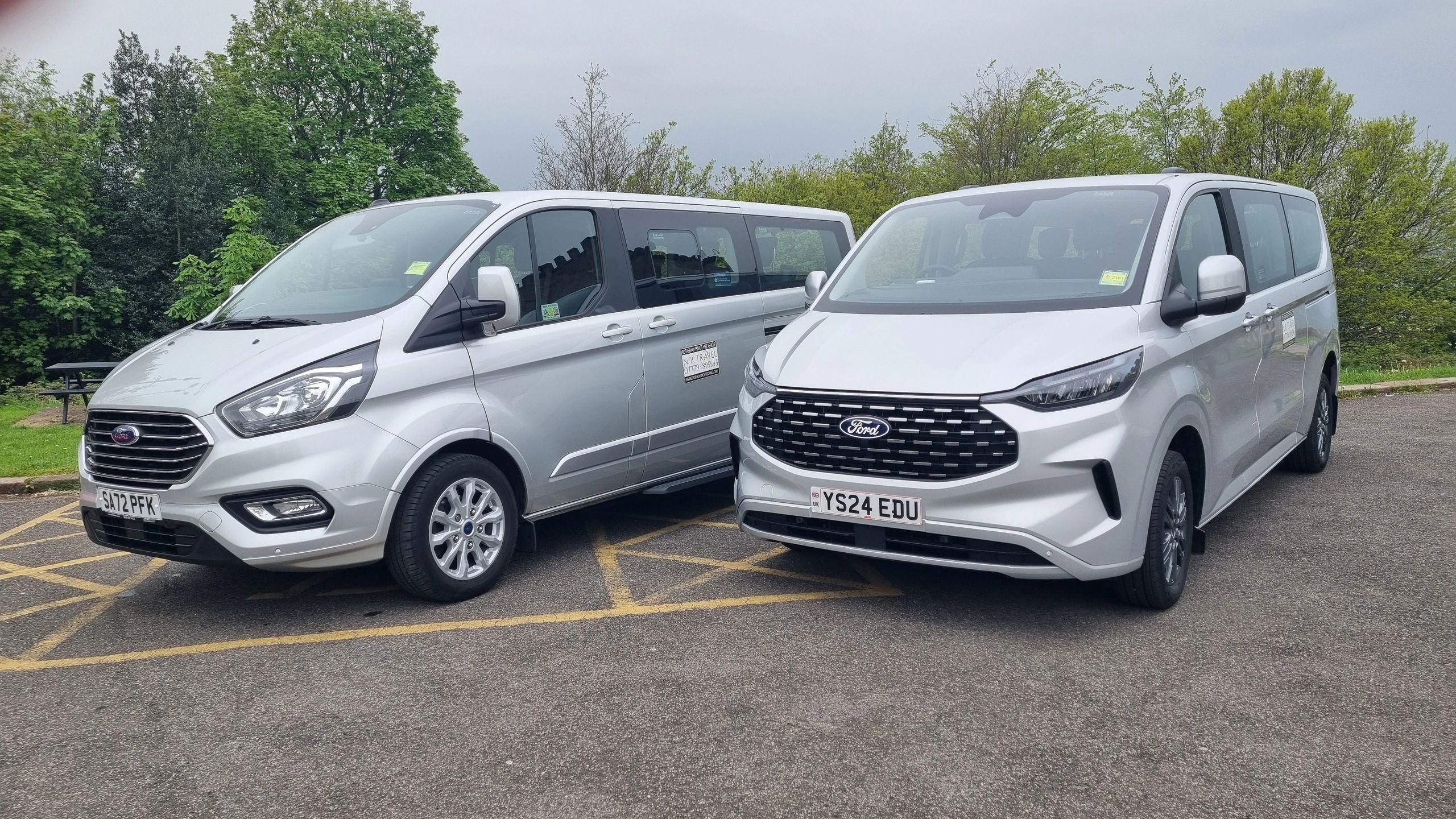 Two silver Ford vans parked side by side in a parking lot.