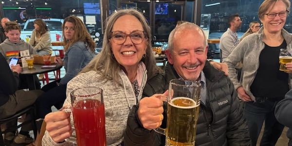 Two people cheer with large drinks in a lively bar setting.