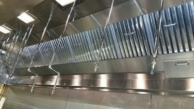 Stainless steel commercial kitchen ventilation hood with exhaust pipes.