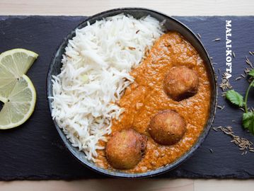 Bowl of white rice with flavorful Malai Kofta curry and lemon slices on the side.