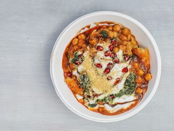 A bowl of rich chickpea curry garnished with yogurt, pomegranate seeds, and herbs.