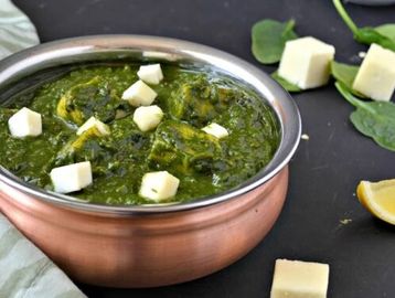A bowl of creamy palak paneer garnished with paneer cubes.