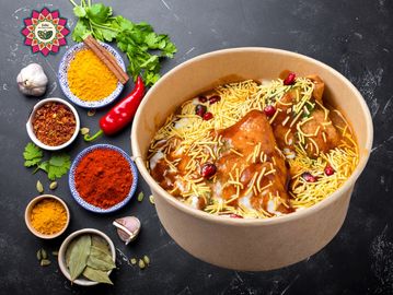 Indian snack chaat with crispy samosas and sev, surrounded by colorful spices.