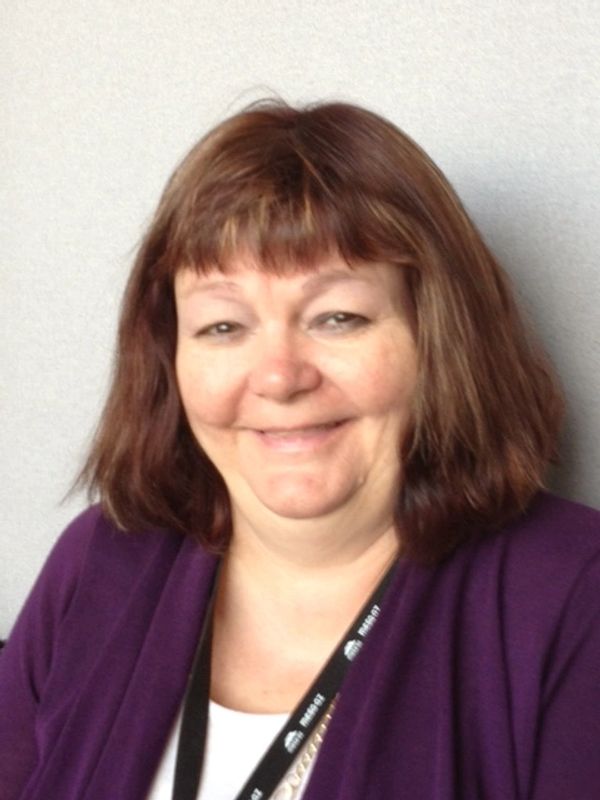 Smiling woman with brown hair and purple cardigan.