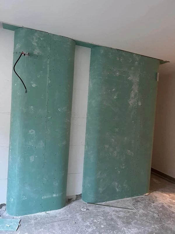 Curved green drywall panels installed on a construction site with exposed wiring.