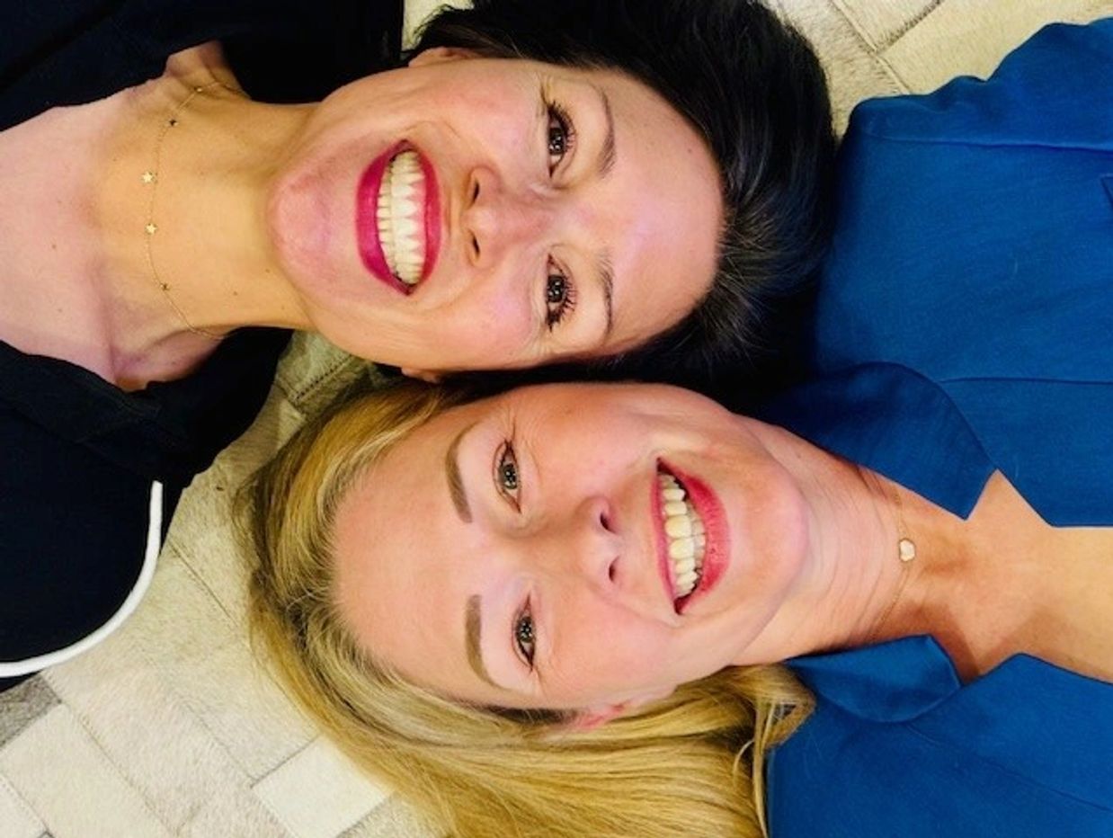 Two women lying down, smiling brightly at the camera.